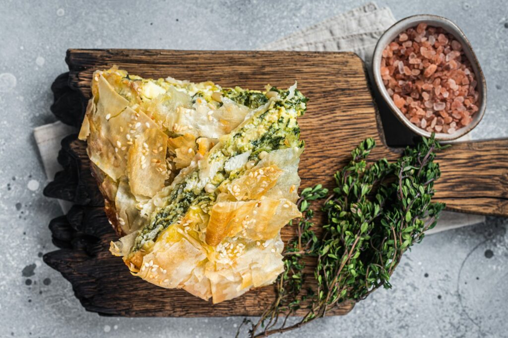 Greek Pie Spanakopita with Spinach and Cheese on wooden board. Gray background. Top view